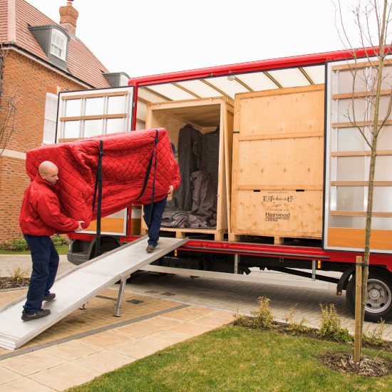 move team staff carrying a red covered sofa onto a lorry