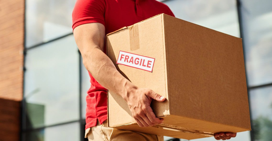 man with red t-shirt carrying a fragile removal box